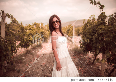 Smiling woman in white dress standing in vineyard 58586110