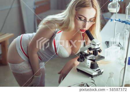 Sexy nurse looking through a microscope. 58587372