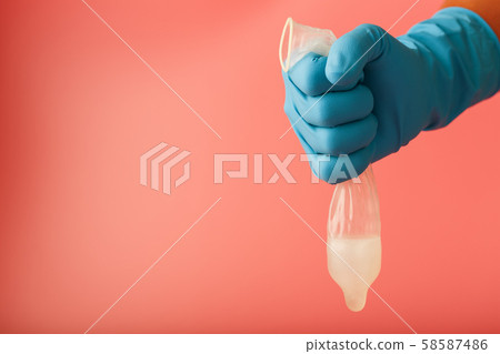 A condom that missed a drop of sperm. A hand in a blue glove holds a used contraceptive on a red A condom that missed a drop of sperm. A hand in a blue glove holds a used contraceptive on a red 58587486