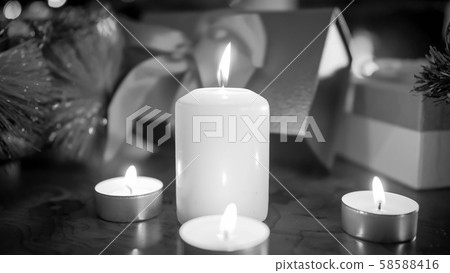 Closeup black and white image of burning candles aginst Christmas gifts and presents Closeup black and white image of burning candles aginst Christmas gifts and presents 58588416