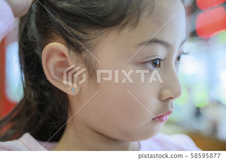 Adorable little Asian girl having ear piercing process. 58595877