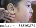 Adorable little Asian girl having ear piercing process. 58595879
