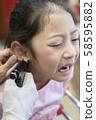 Adorable little Asian girl having ear piercing process. 58595882