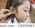 Adorable little Asian girl having ear piercing process. 58595883