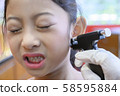 Adorable little Asian girl having ear piercing process. 58595884
