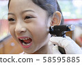 Adorable little Asian girl having ear piercing process. 58595885