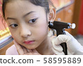Adorable little Asian girl having ear piercing process. 58595889