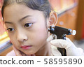 Adorable little Asian girl having ear piercing process. 58595890