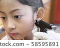 Adorable little Asian girl having ear piercing process. 58595891