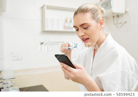 Woman checking phone and brushing teeth 58599423