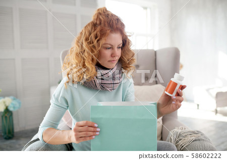 Red-haired woman having flu holding pack of vitamins 58602222