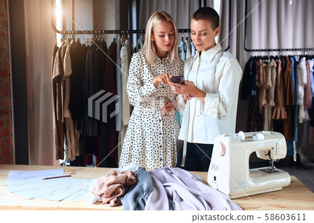 I want such dress. Two attractive women look at each other while designer holding phone I want such dress. Two attractive women look at each other while designer holding phone 58603611