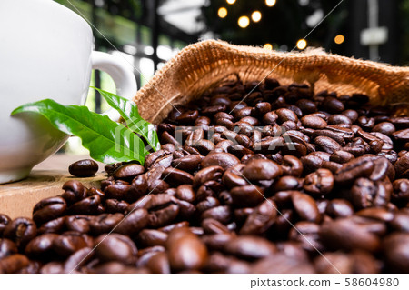 full of coffee beans spilling out bag on brown wooden background with a cup of black coffee 58604980