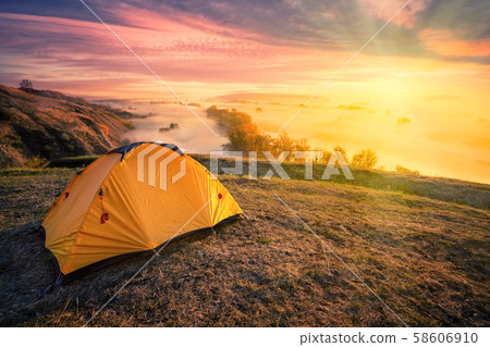 Orange tent on hill above foggy river under bright sun Orange tent on hill above foggy river under bright sun 58606910