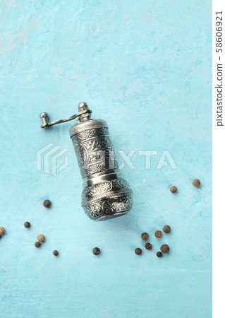 Allspice, Jamaican pepper. Black peppercorns with a vintage pepper mill, top shot on a blue Allspice, Jamaican pepper. Black peppercorns with a vintage pepper mill, top shot on a blue 58606921