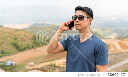 Asian young man using a telephone at a mountain. Asian young man using a telephone at a mountain. 58607417