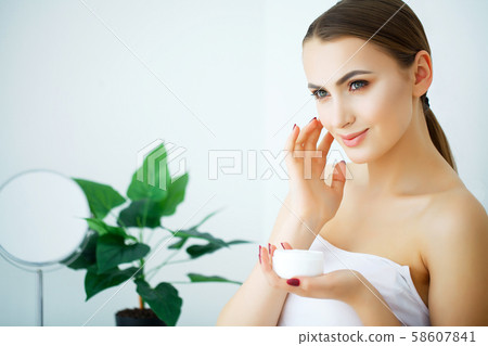 A beautiful woman using a skin care product, moisturizer or lotion and Skincare taking care of her A beautiful woman using a skin care product, moisturizer or lotion and Skincare taking care of her 58607841