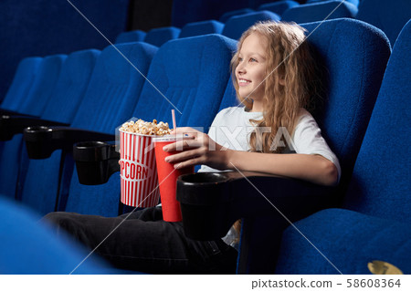 Girl sitting alone in cinema and watching comical movie 58608364