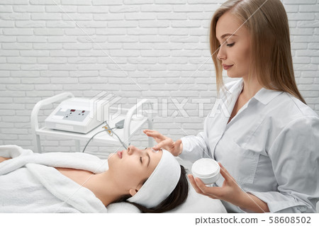 Doctor applying cream on face of young woman. 58608502