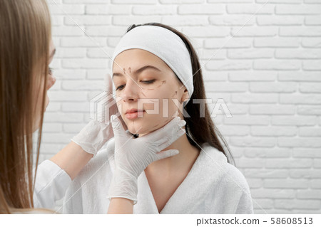 Woman with marked black lines on face and cosmetologist. Woman with marked black lines on face and cosmetologist. 58608513