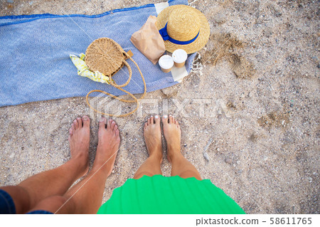 Picnic near the sea. A blue plaid on which are glasses with coffee, a bag, a hat. Feet of a couple 58611765
