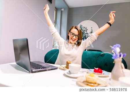 Portrait of beautiful smiling woman in glasses in winning pose sitting in a cafe with laptop indoors Portrait of beautiful smiling woman in glasses in winning pose sitting in a cafe with laptop indoors 58611978