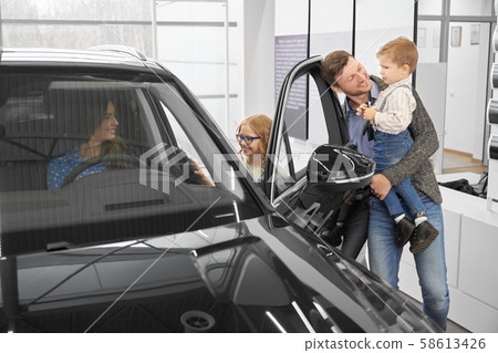 View from side of happy family looking at car in auto salon View from side of happy family looking at car in auto salon 58613426