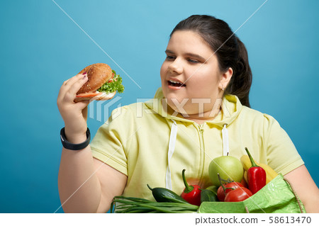 Chunky female trying to eat burger instead of healthy food 58613470