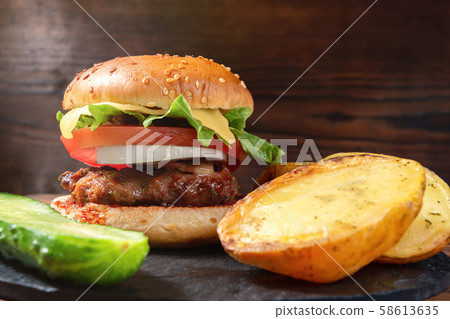 Fresh homemade burger and baked potatoes with cucumber on a slate dish on a wooden background 58613635