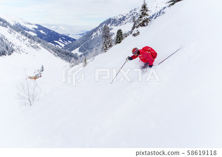 Side photo of athlete man in red jacket and with backpack skiing in winter resort 58619118
