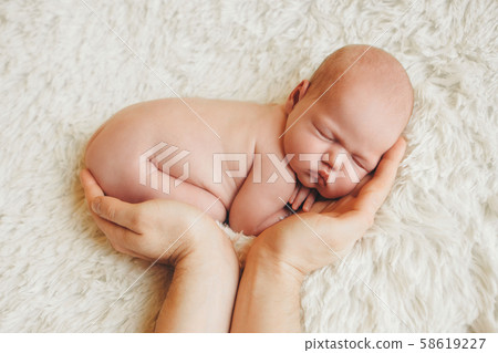 naked newborn baby lying on the hands of parents on a white background. Imitation of a baby in the womb. beautiful little girl sleeping lying on her stomach. 58619227
