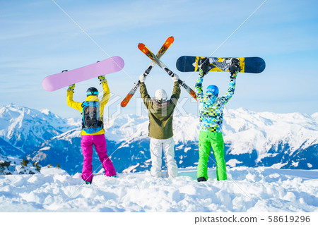 Photo from behind of three athletes with arms raised with snowboards and skis on day . Photo from behind of three athletes with arms raised with snowboards and skis on day . 58619296