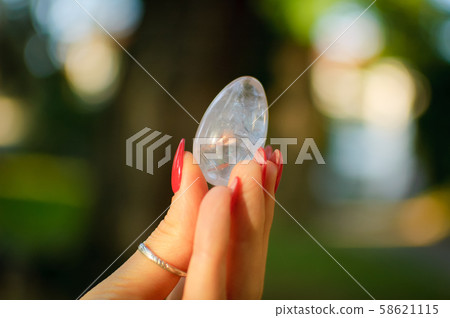 Female hand with transparent amethyst quartz yoni egg for vumfit, imbuilding or meditation. Shining Female hand with transparent amethyst quartz yoni egg for vumfit, imbuilding or meditation. Shining 58621115