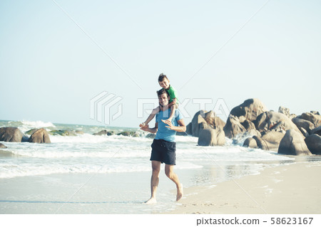 happy family on beach playing, father with son walking sea coast, rocks behind smiling taking 58623167