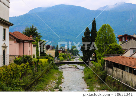 Picturesque italian town Mandello with lovely houses, trees and Alps in background. 58631341