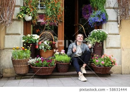 Young boy keeping smartphone and sitting at flower shop near bouquets in baskets. 58631444