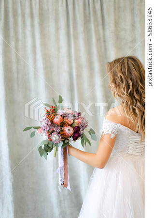 Back view of young caucasian bride standing at photo studio with flowers. 58633146