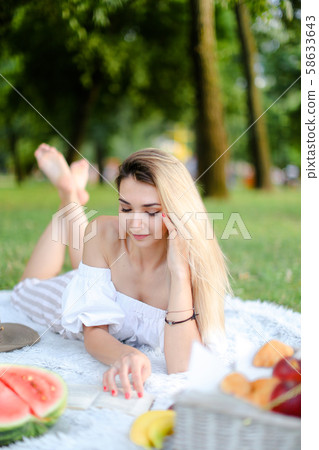 Young woman lying on plaid in park and reading book. 58633643