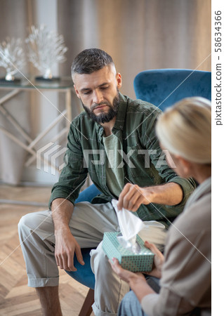Bearded stylish man taking napkin while visiting psychologist Bearded stylish man taking napkin while visiting psychologist 58634366