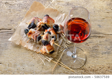 Delicious Spanish tapas: Fried prunes wrapped in bacon with a glass of red wine 58637589