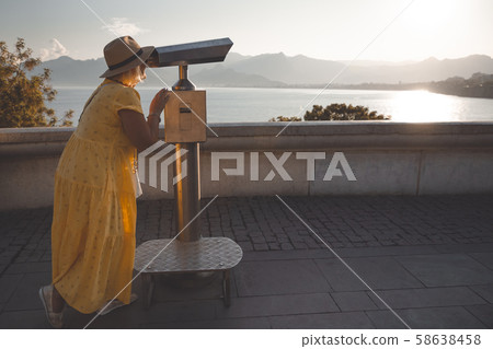 Mature female traveler looks through tourist binocular at mountains and sea. Concept of traveling 58638458