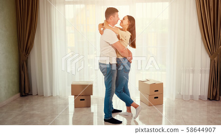 couple wearing blue jeans hugs kisses in middle of new house 58644907