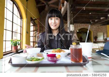 An Asian woman is by the window of the restaurant. 58645250
