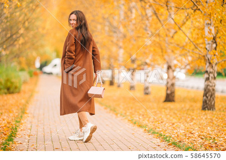 Fall concept - beautiful woman drinking coffee in autumn park under fall foliage Fall concept - beautiful woman drinking coffee in autumn park under fall foliage 58645570