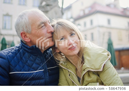 Handsome elderly man is embracing his young blonde wife spending time together outdoors in the Handsome elderly man is embracing his young blonde wife spending time together outdoors in the 58647936