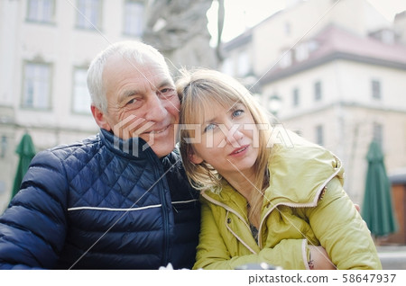 Handsome elderly man is embracing his young blonde wife spending time together outdoors in the Handsome elderly man is embracing his young blonde wife spending time together outdoors in the 58647937