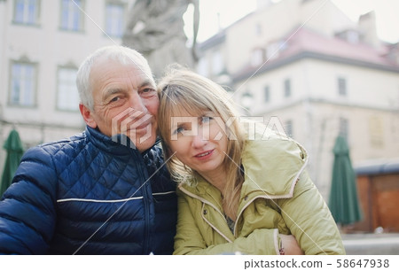 Handsome elderly man is embracing his young blonde wife spending time together outdoors in the Handsome elderly man is embracing his young blonde wife spending time together outdoors in the 58647938