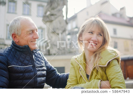 Handsome elderly man is embracing his young blonde wife spending time together outdoors in the Handsome elderly man is embracing his young blonde wife spending time together outdoors in the 58647943