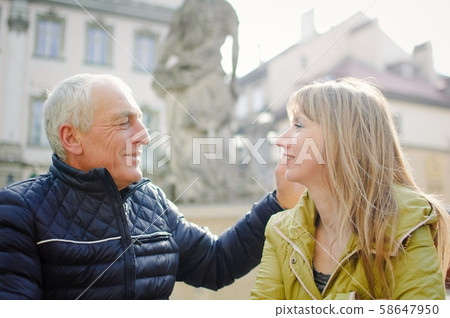Handsome elderly man is embracing his young blonde wife spending time together outdoors in the Handsome elderly man is embracing his young blonde wife spending time together outdoors in the 58647950