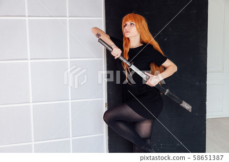 Woman cosplayer anime with red hair holds a Japanese sword Woman cosplayer anime with red hair holds a Japanese sword 58651387